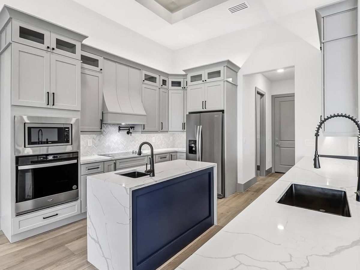 Cocina remodelada con gabinetes grises, isla azul marino y encimeras de cuarzo blanco
