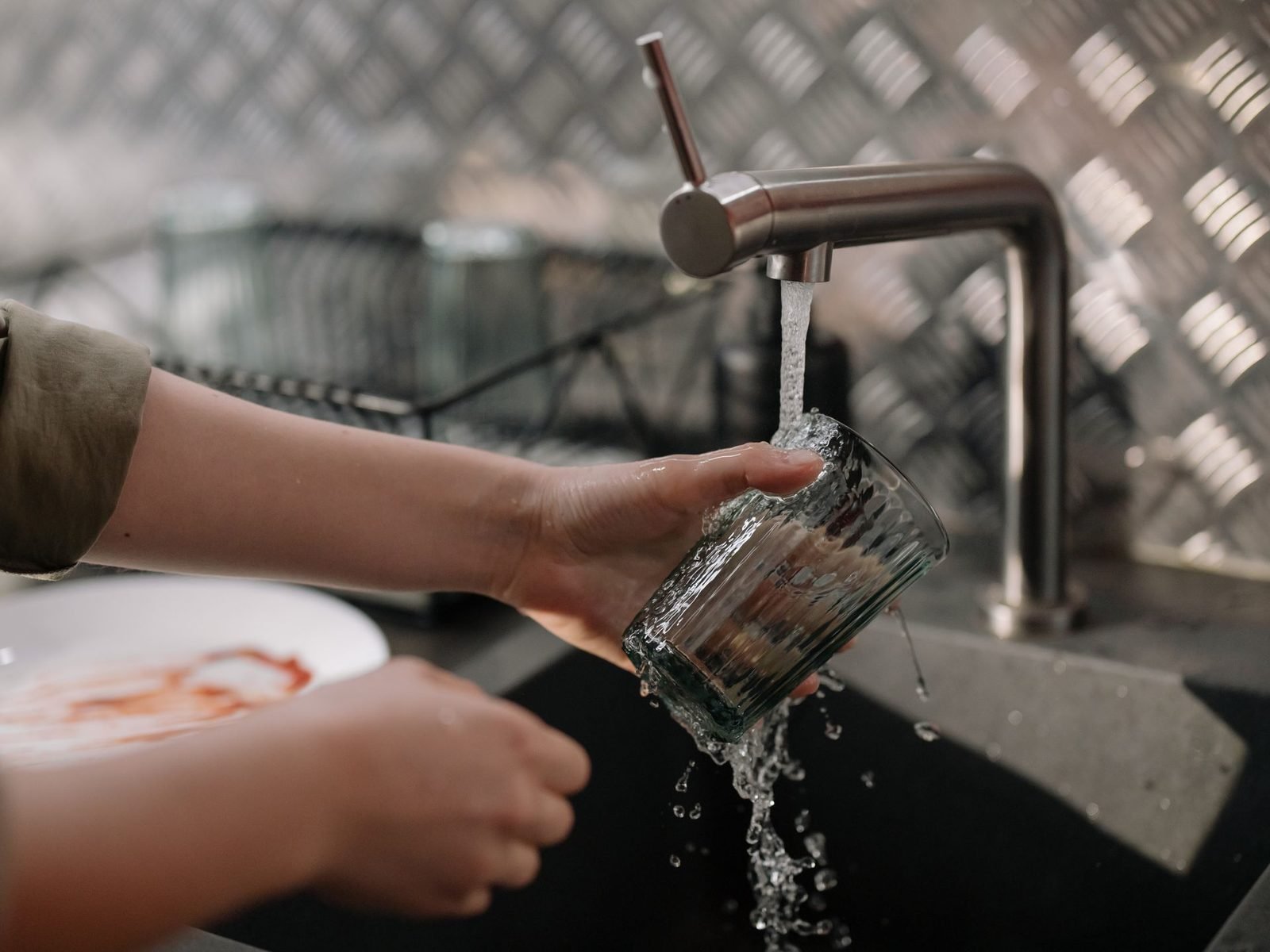 Manos llenando un vaso con agua del grifo de la cocina